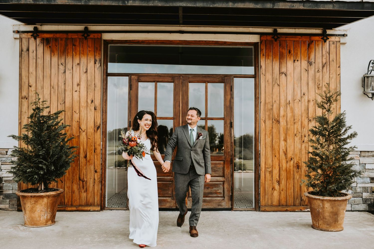 an elegant bride and groom hold hands and walk in front of the barn doors at oak and ivy wedding venue