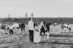 Black and white photo of a couple standing among grazing horses in an open field.