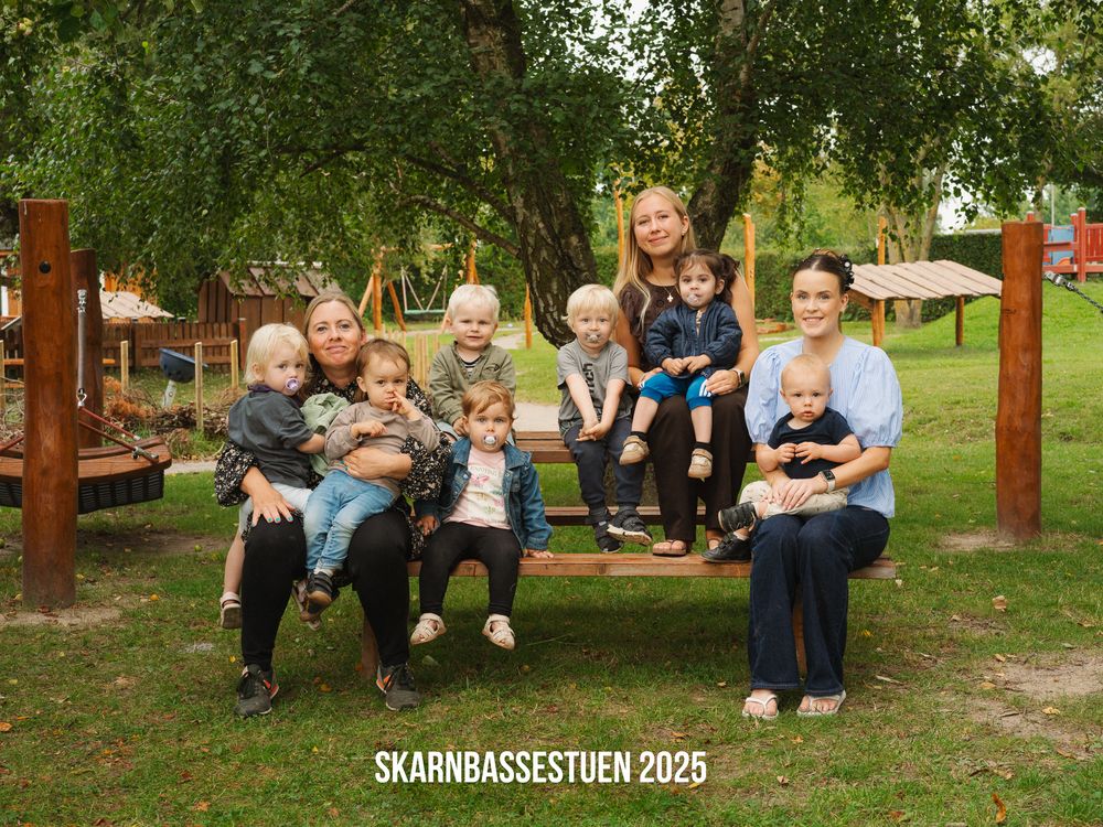 A row of people sitting on wooden benches in an outdoor garden or park setting.
