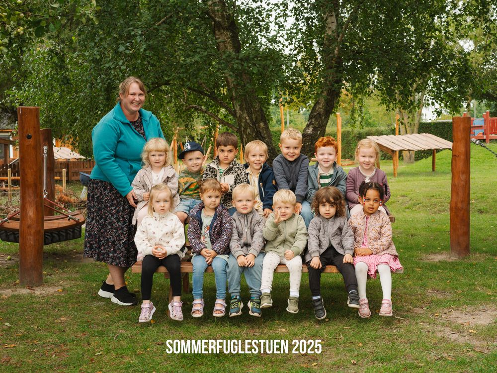 Large group of children and adults gathered on wooden benches in a park setting during summer activities.
