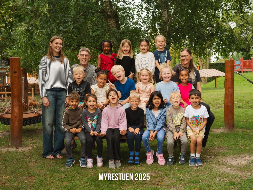 A group of young children sitting together on wooden benches outdoors in a wooden playground setting.