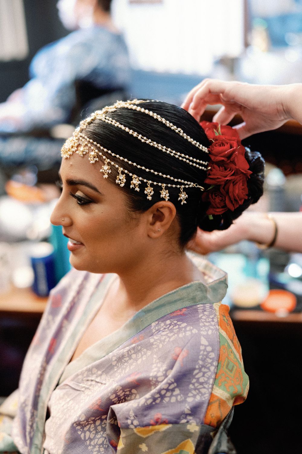 Indian bride getting gold maang tikka hair jewelry styled for her wedding ceremony.