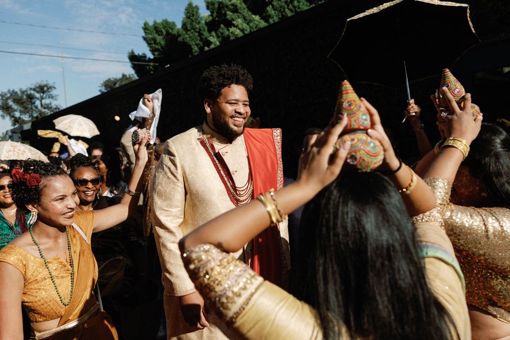 Groom in gold sherwani celebrating joyful baraat procession with dancing guests.