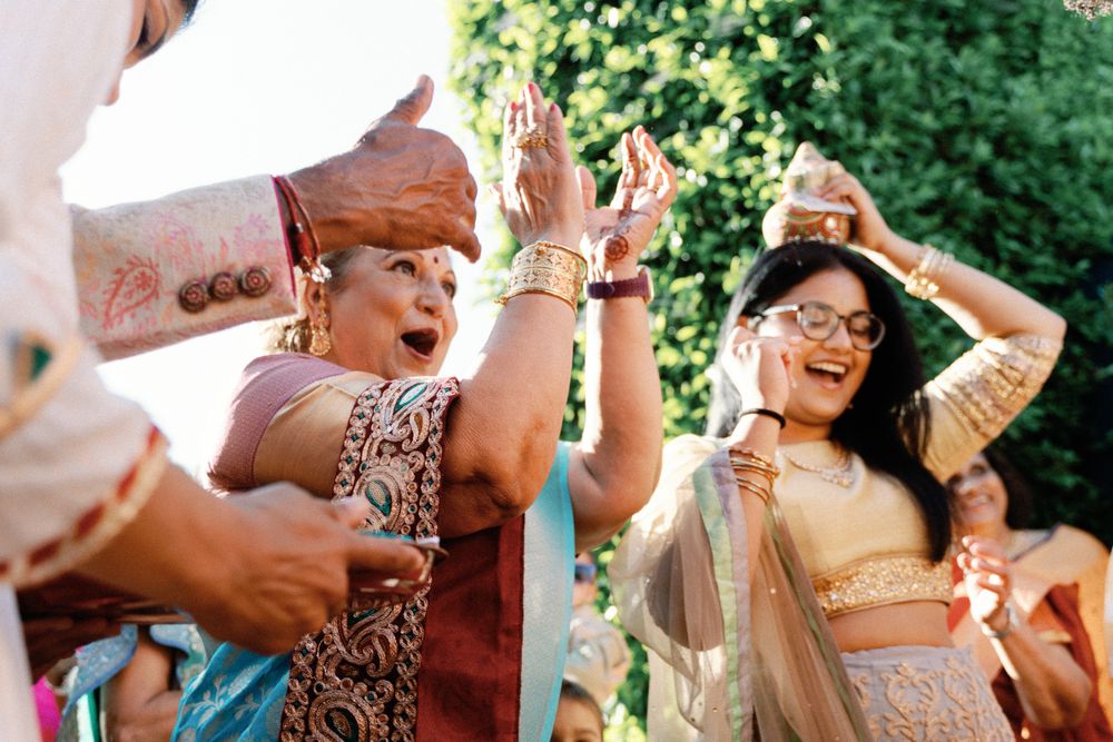 Guests in gold lehengas dancing joyfully during outdoor Indian wedding baraat.