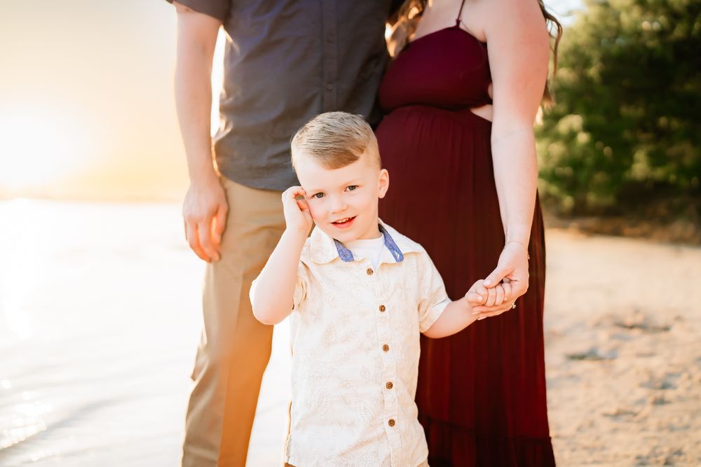 A couple walks with their baby at sunset along a sandy path through a natural outdoor setting.