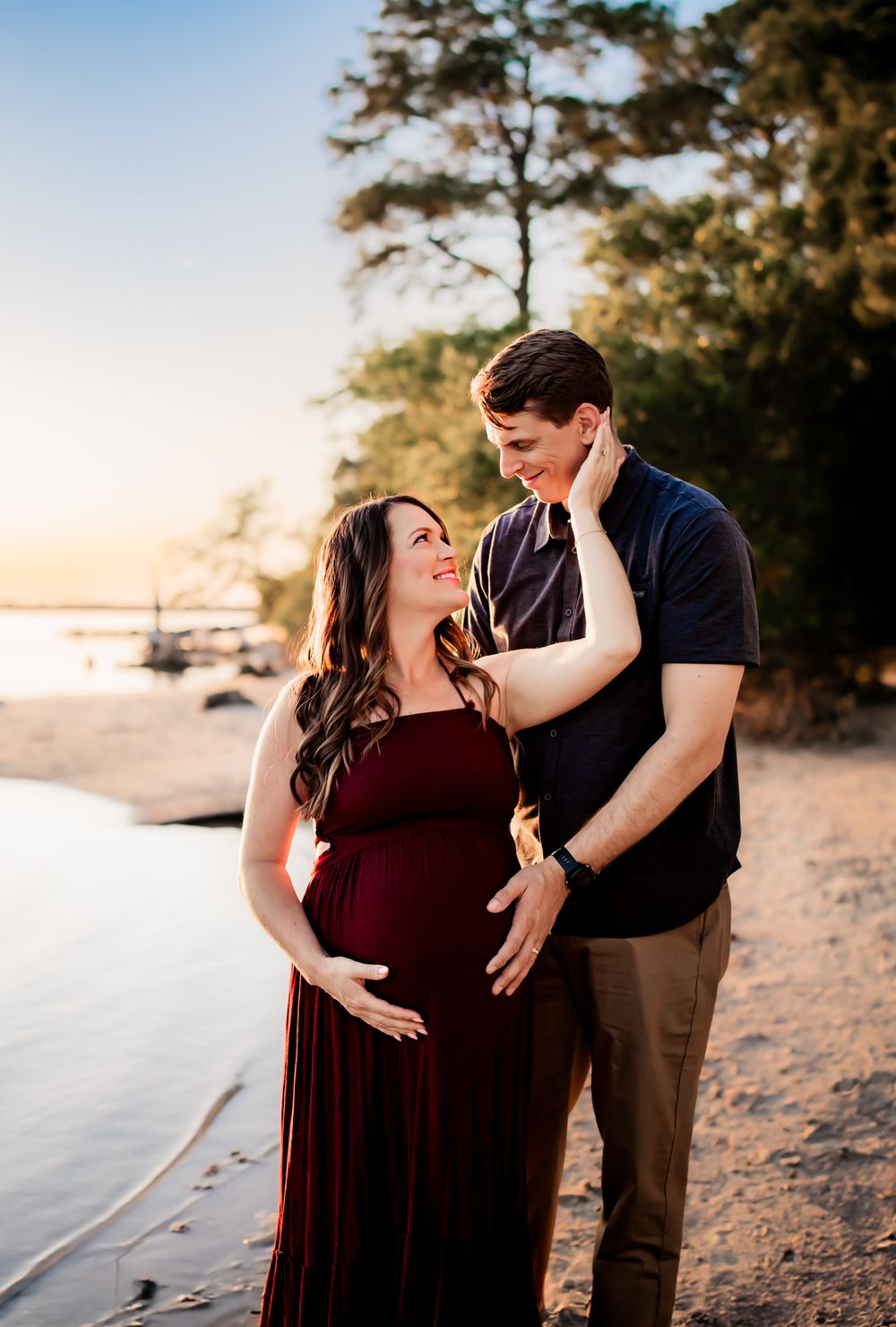 A couple shares intimate moments during a romantic sunset beach photoshoot while wearing burgundy and navy outfits.