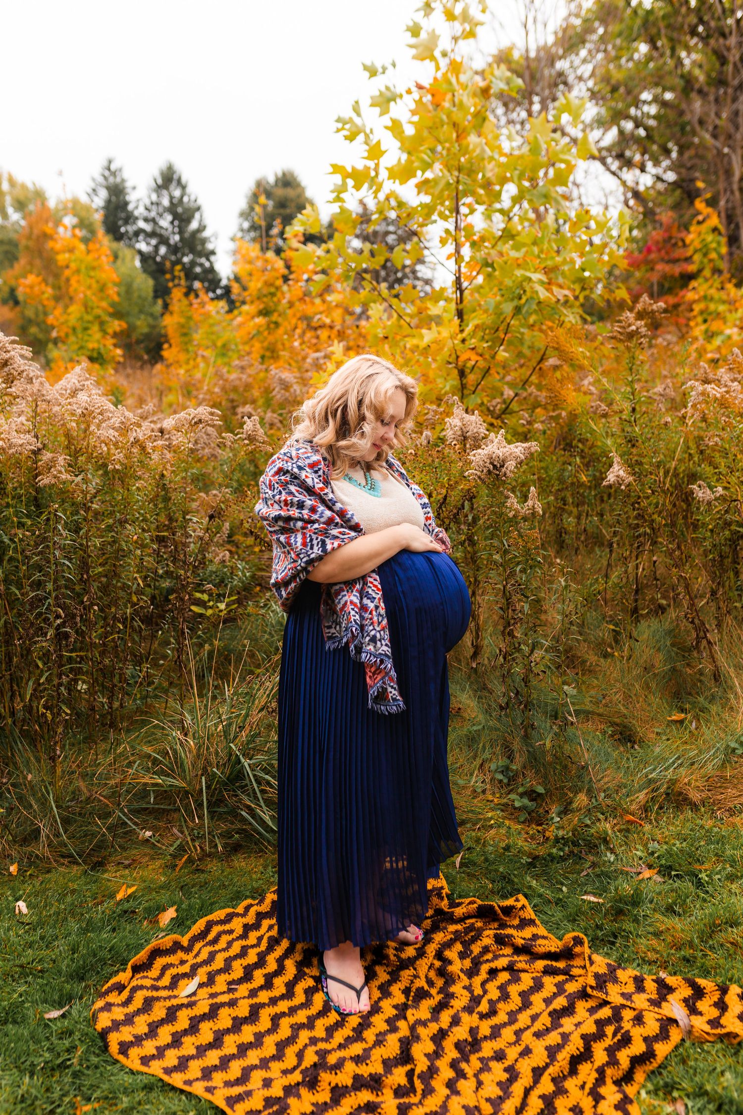 Expecting mom in cozy shawl caresses her belly during fall maternity session in Oxford County