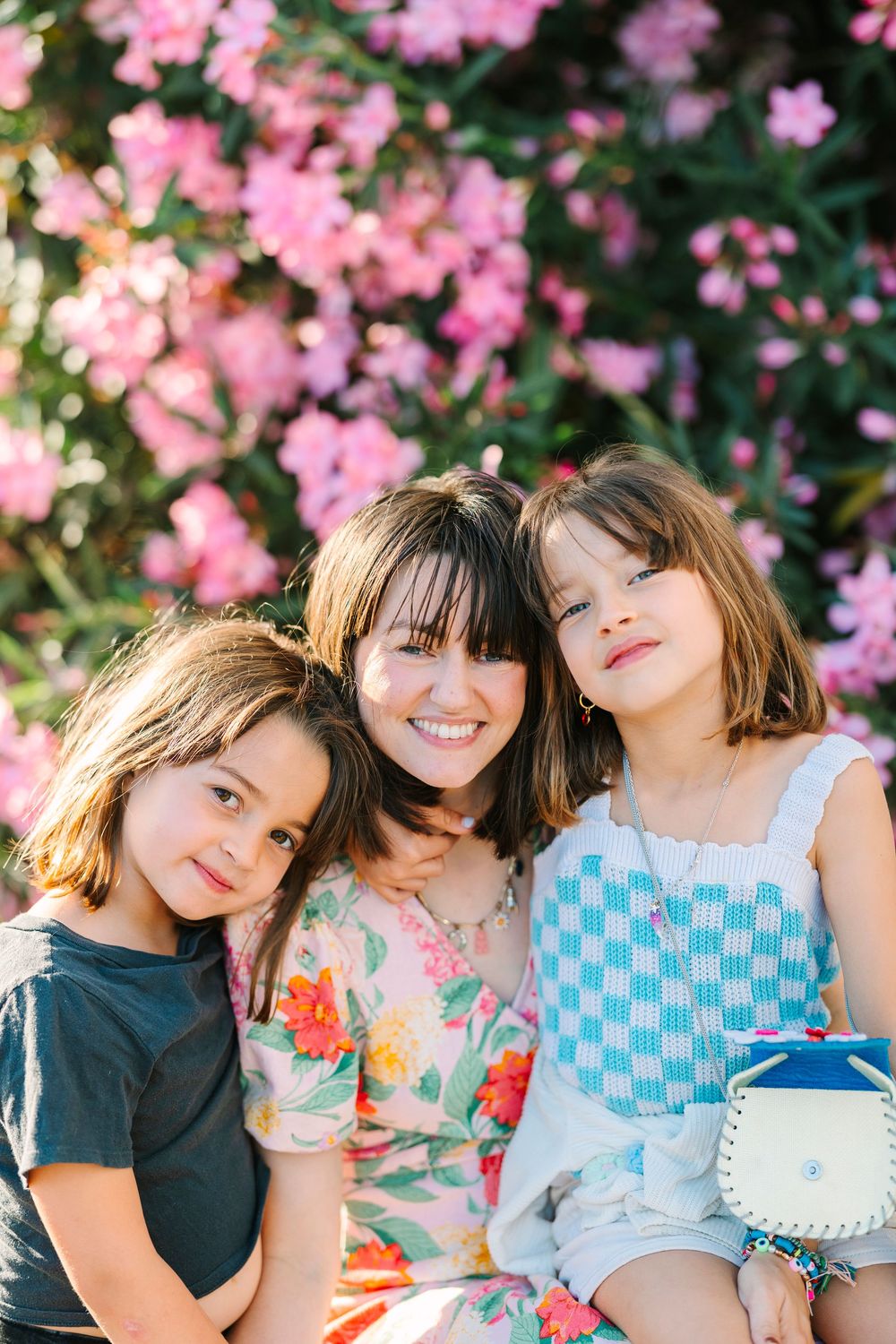 Three smiling figures pose together against a backdrop of pink cherry blossoms in full bloom.