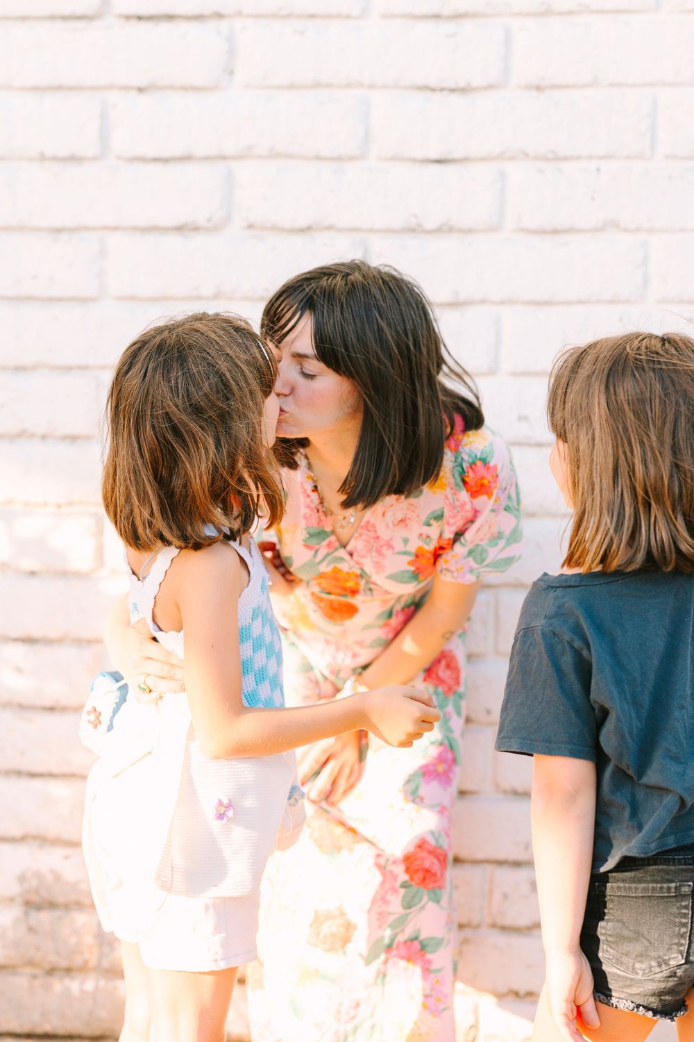 Intimate family moment captured against white brick wall background.