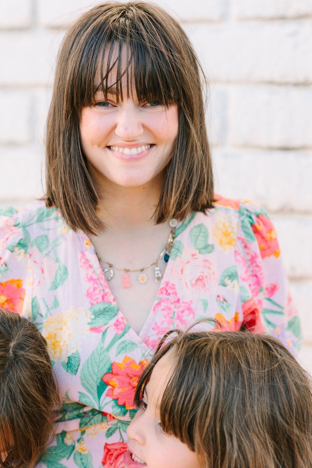 Close-up portrait of person in floral dress with bangs smiling brightly.