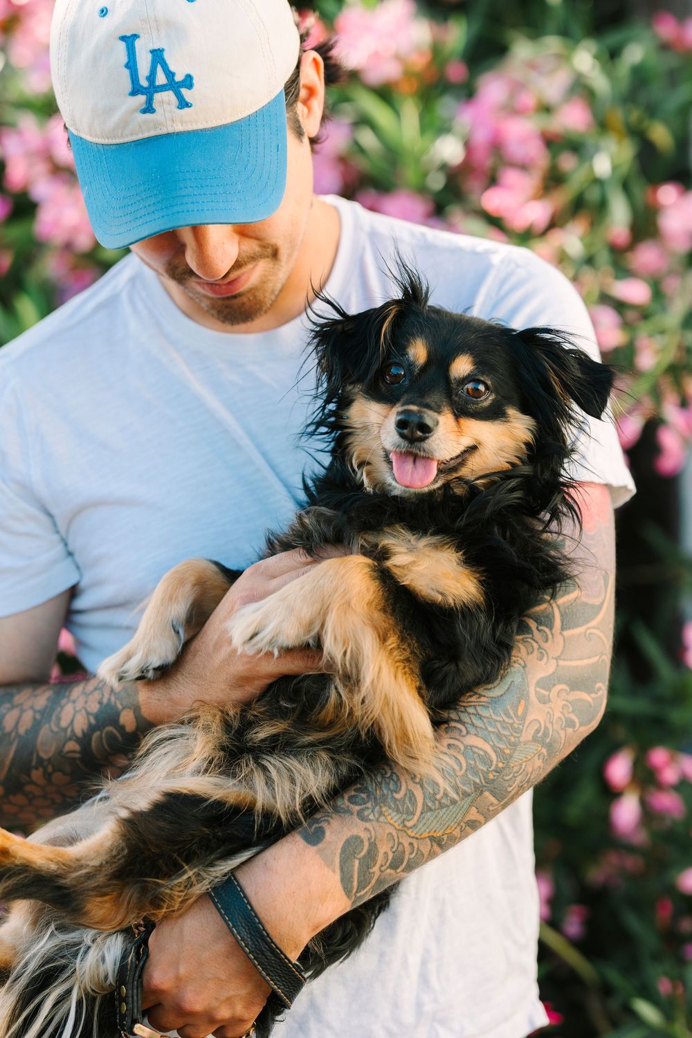 Person in LA cap holds happy black and tan dog against pink floral background.