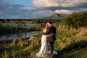 Romantic figures share intimate moments in a rustic outdoor setting as sunlight glows across grassy fields and water.