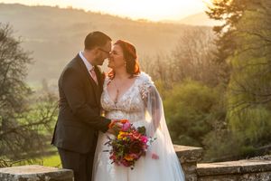 Bride and groom share a romantic moment at golden hour, with lush green hills and warm sunset light in the background.