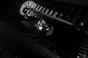 Black and white photo of a person wearing a mask lying near dark train tracks in dramatic lighting.