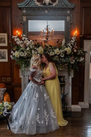 An elegant wedding scene with floral decorations adorning a fireplace mantel, featuring a chandelier and glowing candles.