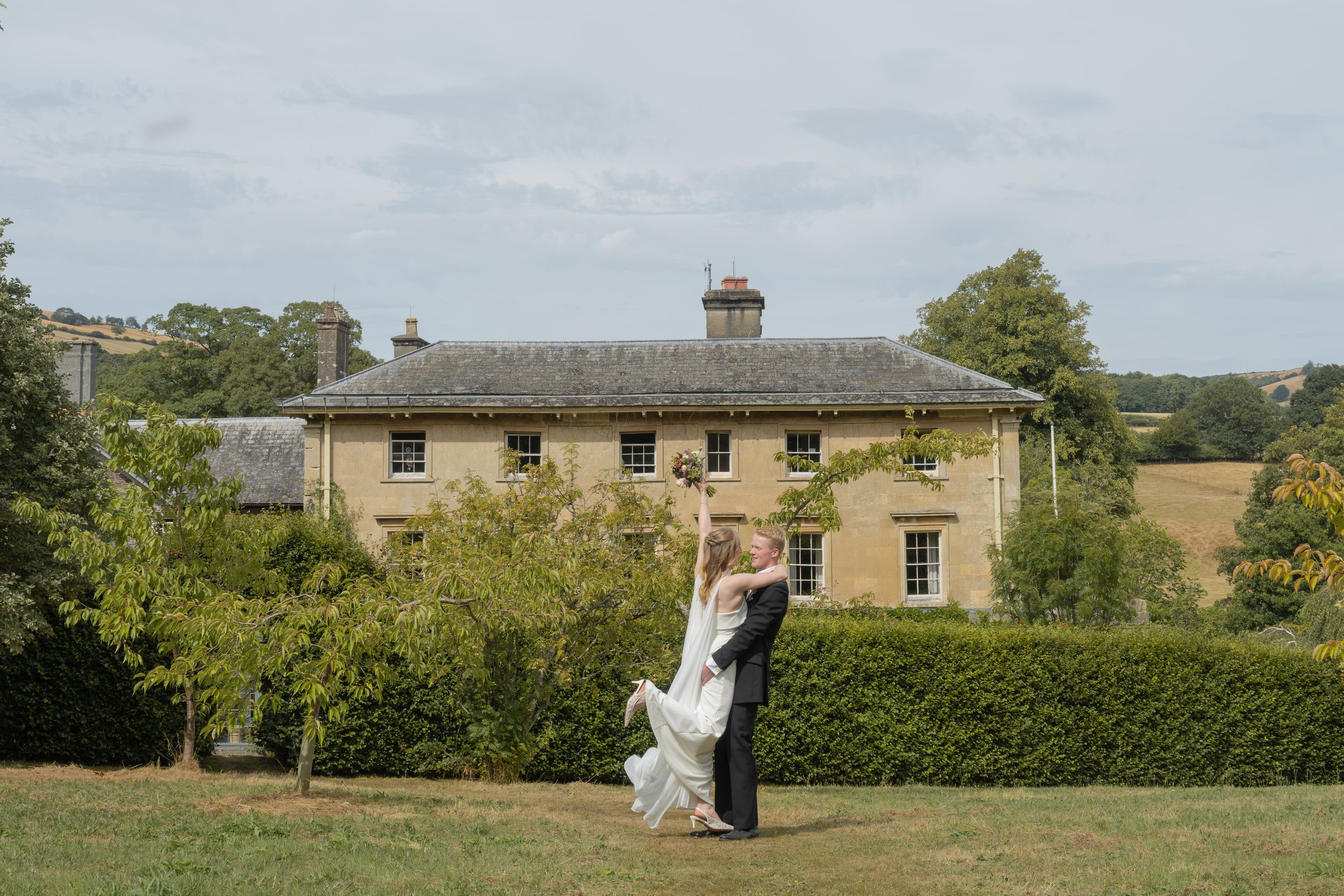 Bride and groom dancing on lawn before grand country house estate on their wedding day.