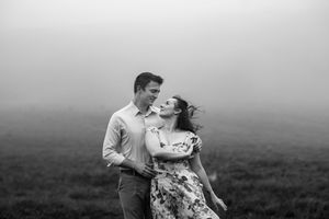 Black and white misty engagement photos on a mountaintop with couple embracing in romantic poses at sunset.