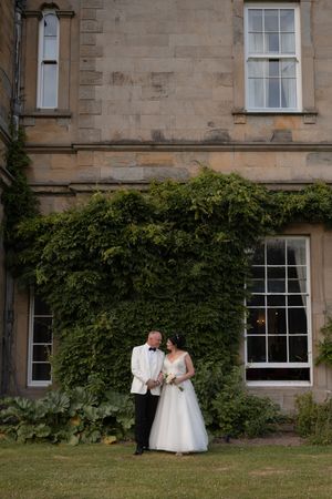 Bride and groom standing together in front of a ivy-covered stone mansion on their wedding day.