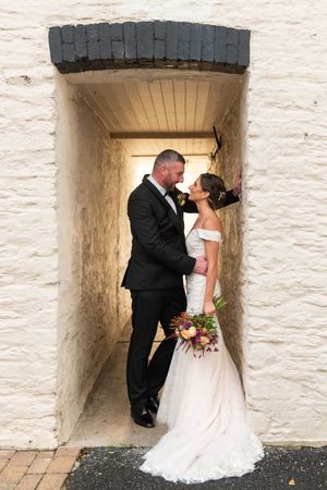 A bride and groom share intimate moments in a white stone archway during their wedding photoshoot.