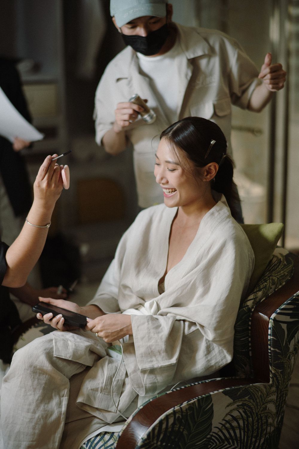 A person in a white robe sitting in a chair and laughing during a getting ready session.
