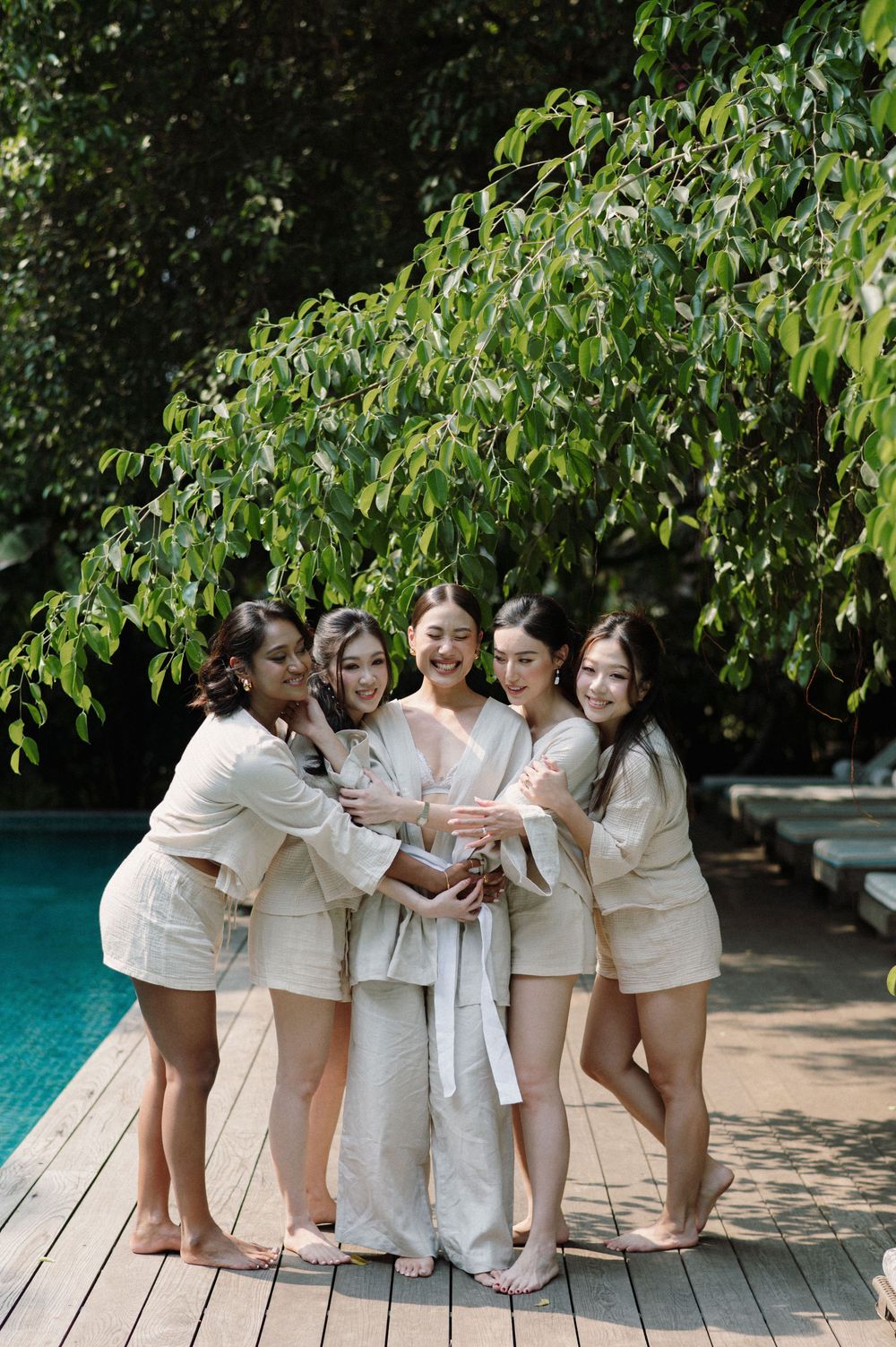 A group wearing matching white outfits sits together by a pool deck surrounded by green trees.