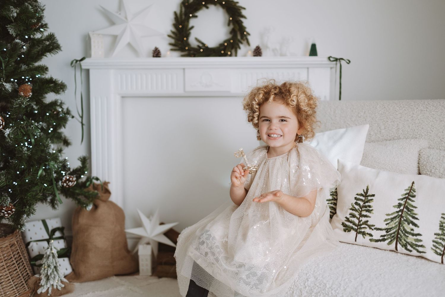 Family with young children wearing white outfits poses together in bright white room.