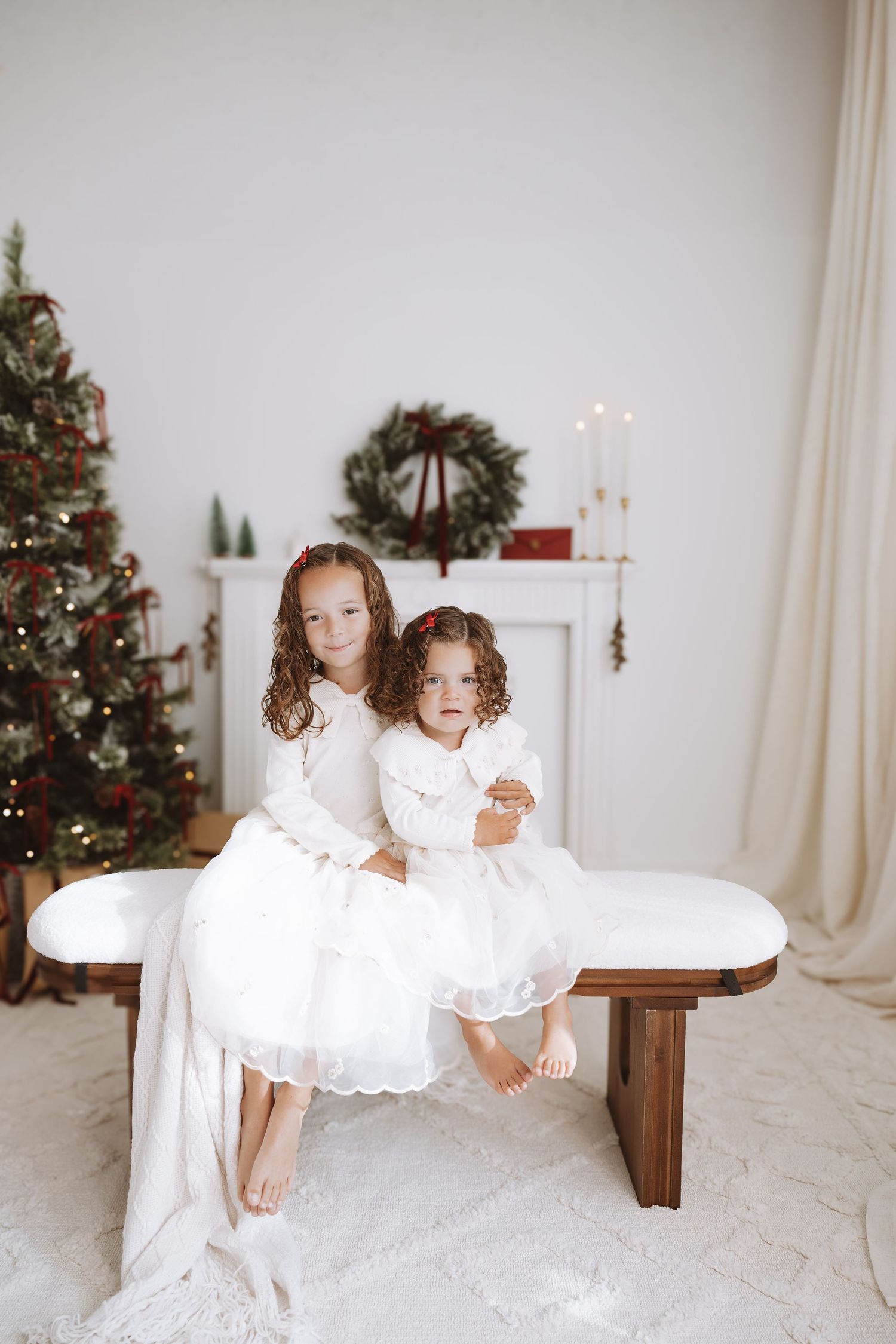 Family with young children wearing white outfits poses together in bright white room.