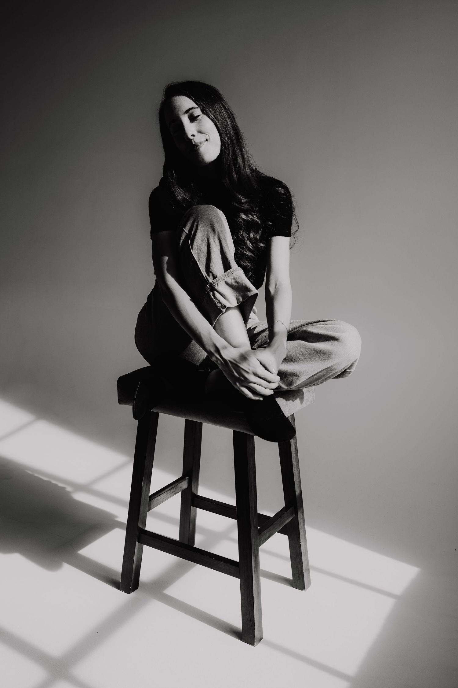 Artistic black and white portrait of person seated on wooden stool.