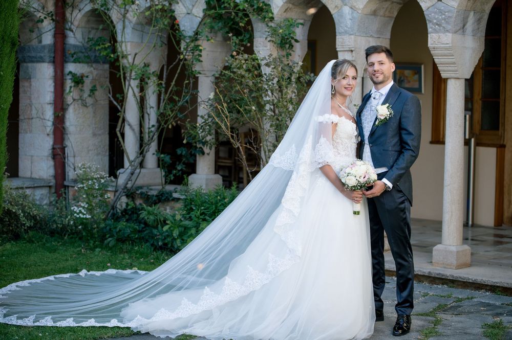 Elegant wedding couple posing in stone archway courtyard with flowing veil.