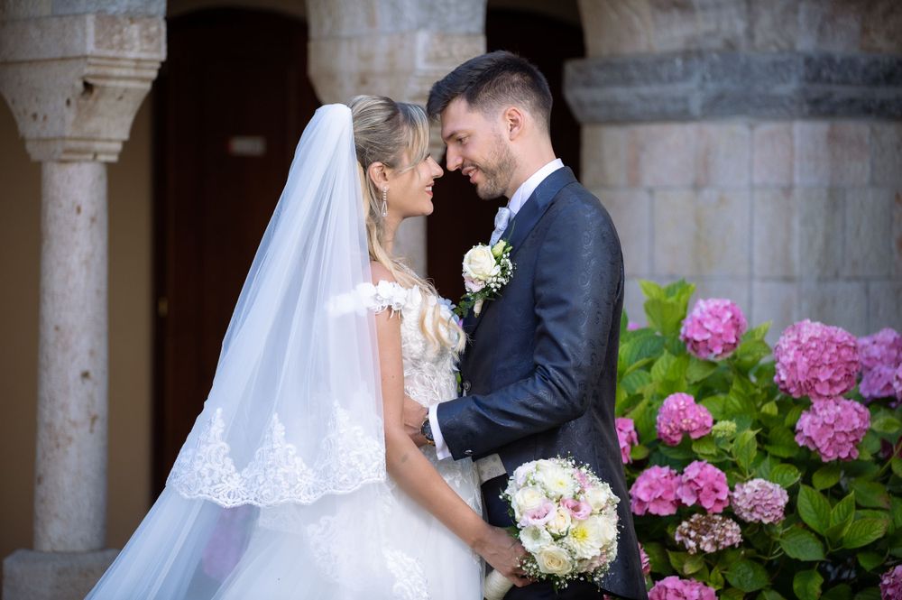 Bride and groom portrait with stone columns and pink hydrangeas in background.