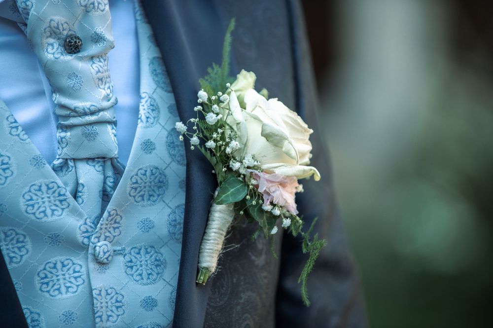 Close-up detail of light blue patterned vest and boutonniere at formal wedding.