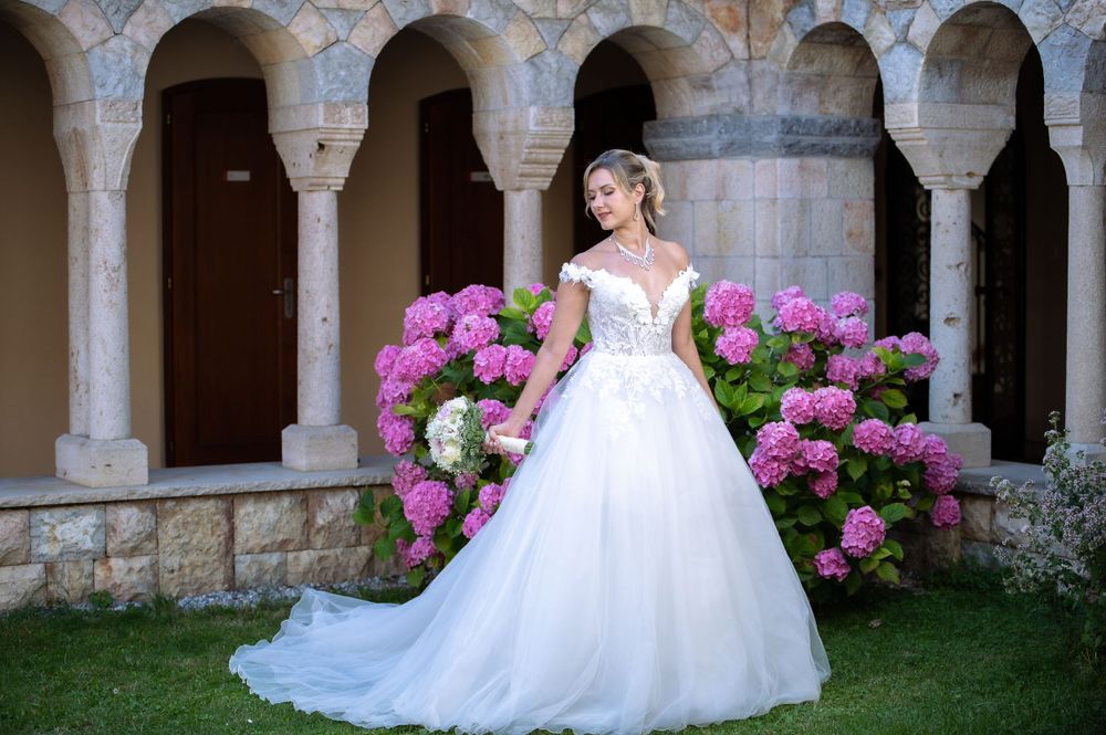 Stone colonnade with arches provides romantic backdrop for wedding photos with vibrant pink flowers.