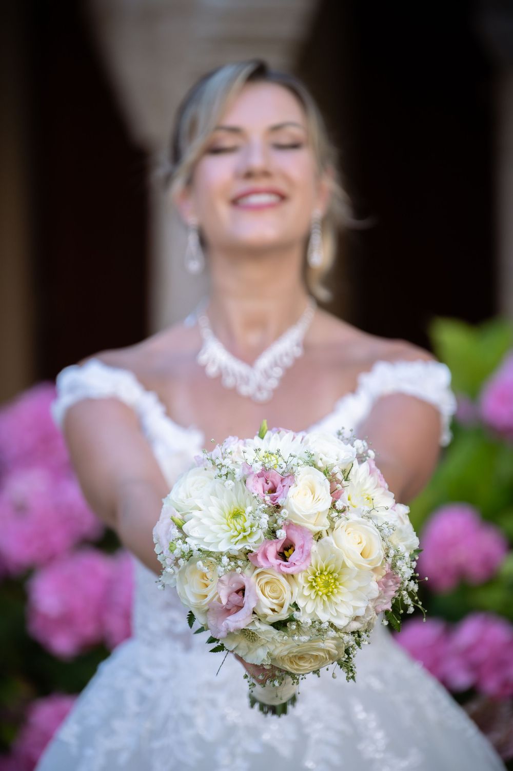 Bridal bouquet featuring soft pink and white roses with delicate greenery against lace dress.