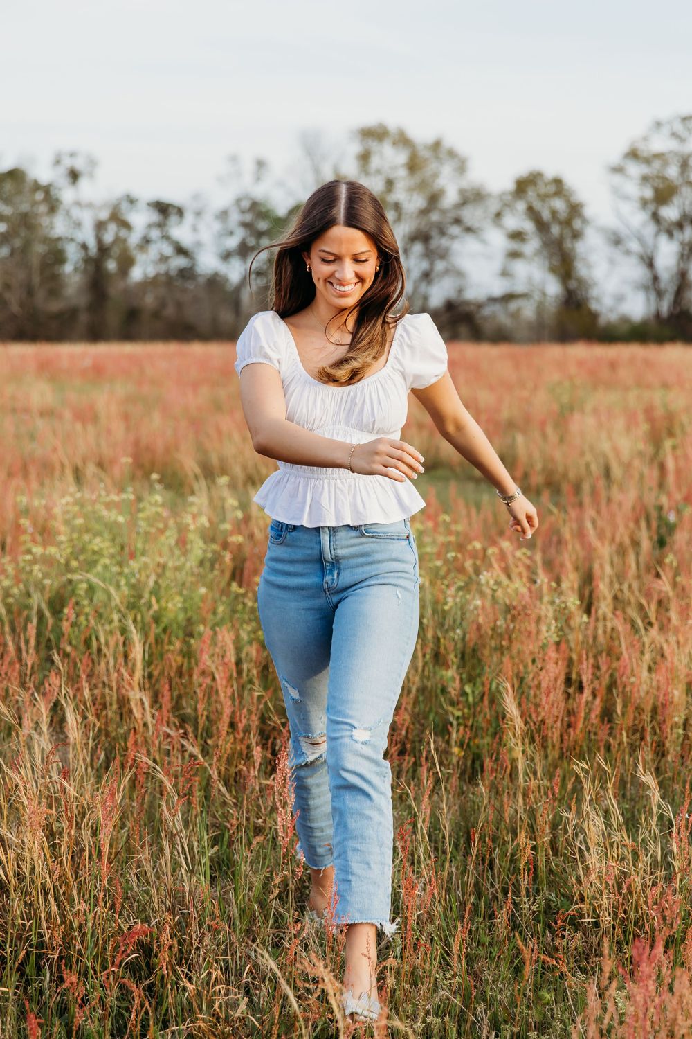 A person in light denim and white top walks through a field of red wildflowers on a sunny day.