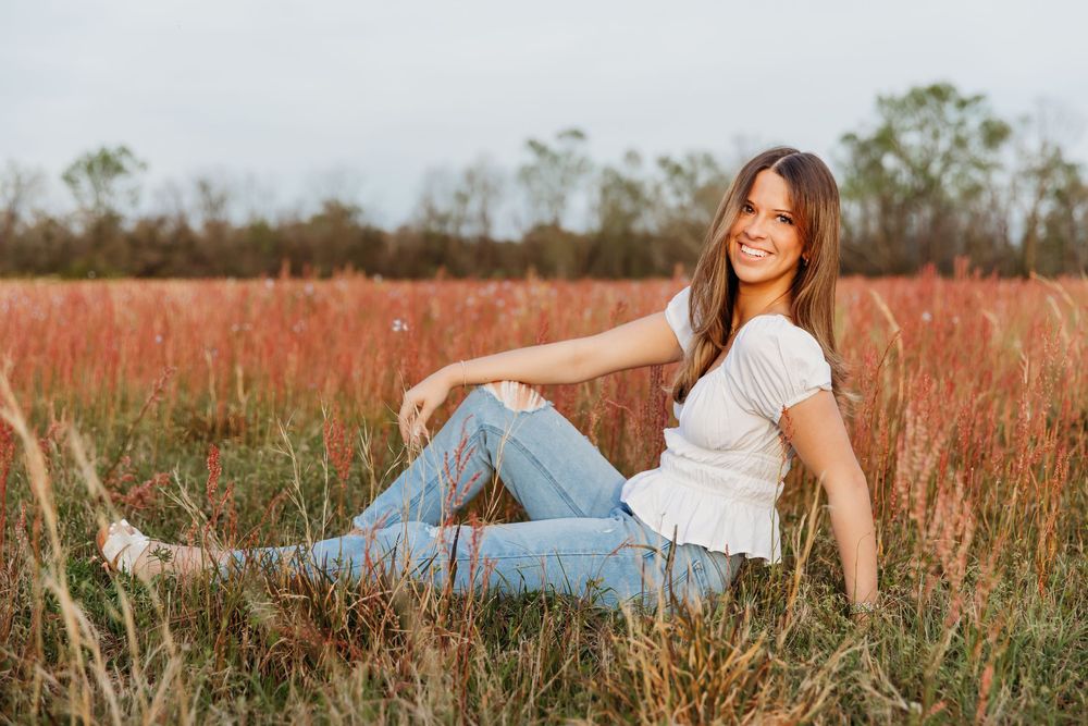 A person wearing denim jeans and white top lounges casually in a rustic golden grass field during autumn.