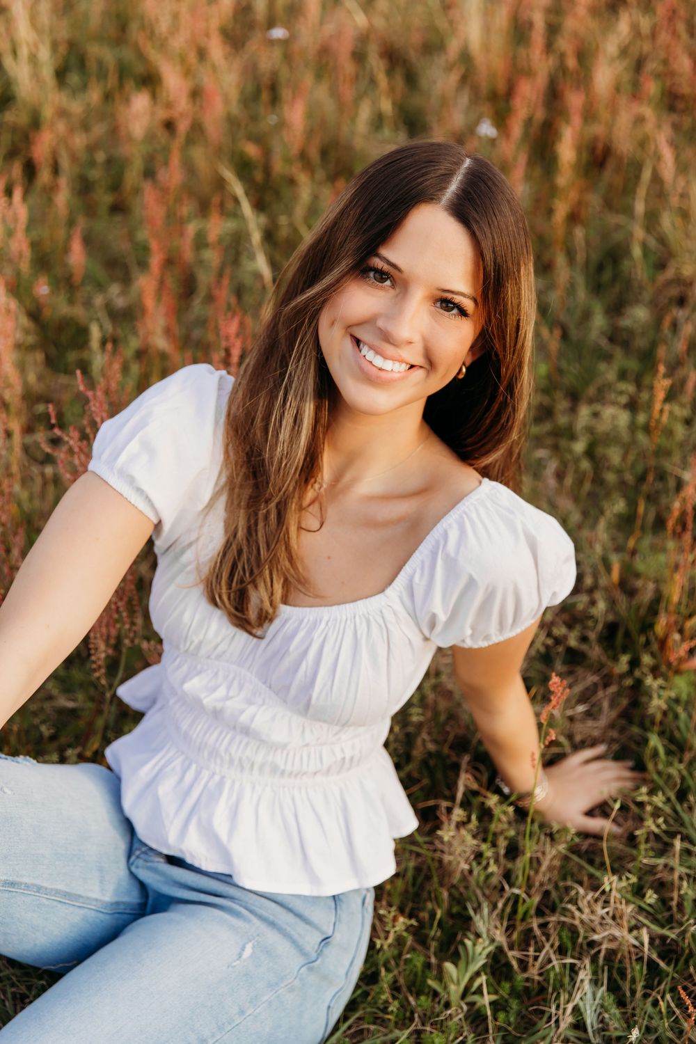 Portrait in a field showing bright smile wearing white ruffle top and light denim jeans at golden hour.