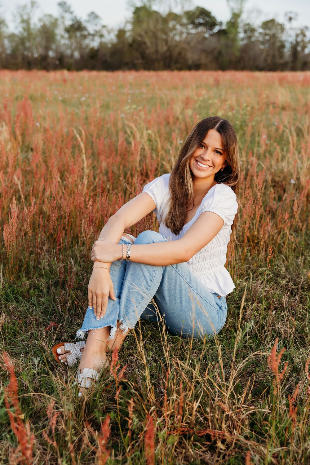 A joyful outdoor portrait in a field of tall reddish grass during golden hour wearing casual denim and white.