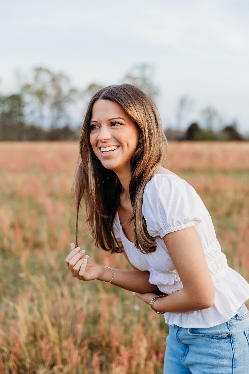 A joyful person poses playfully in a field of tall autumn grasses on a bright day.