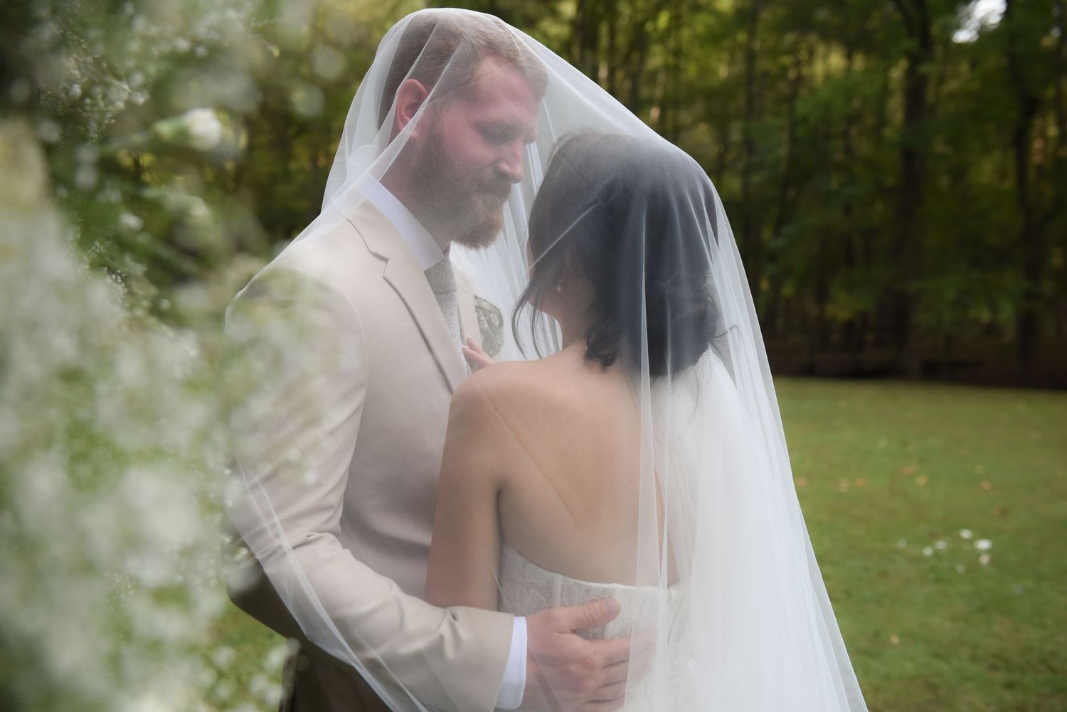 Ethereal wedding moment captured through sheer veil in natural outdoor setting.