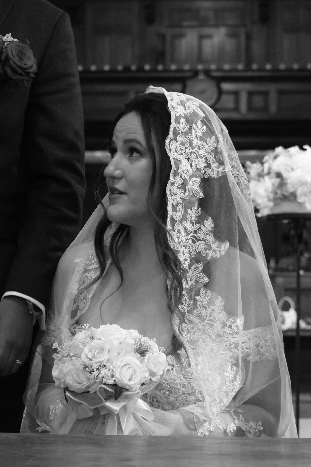 A bride in a beautiful lace veil holds a white rose bouquet during her black and white wedding portrait.