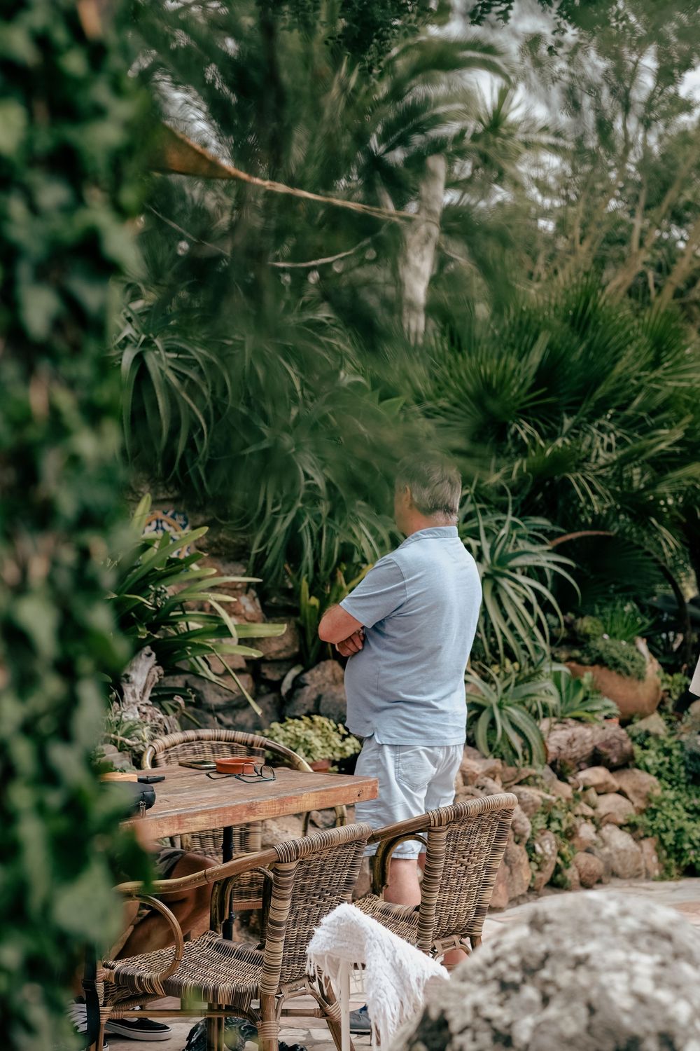 A series of five connected photos showing a person in light clothing sitting on outdoor wooden and wicker furniture in a garden setting.