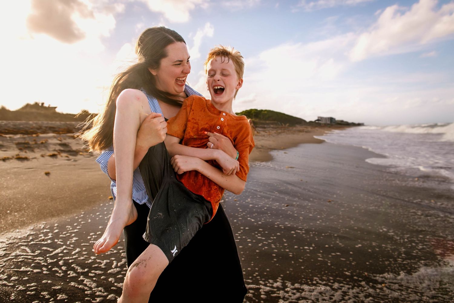 A joyful moment of laughter and play on a scenic beach during sunset with waves crashing on the shore.