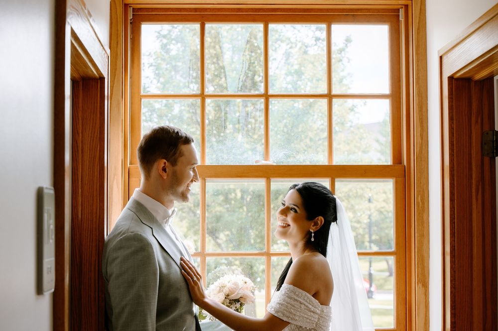 A wedding couple shares an intimate moment by a bright window in warm natural light.