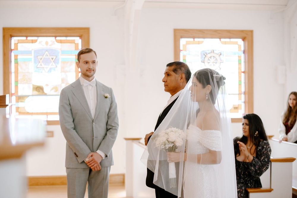 A wedding ceremony in progress inside a chapel with stained glass windows and wooden accents.
