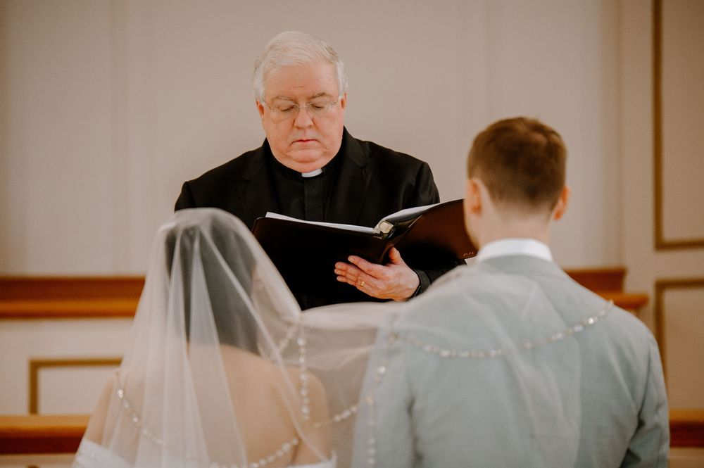 A wedding ceremony officiant reads from a book during an intimate indoor service.