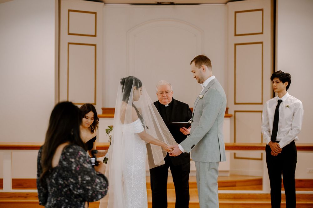 An intimate wedding ceremony scene in a simple white room with attendees gathered around the couple.