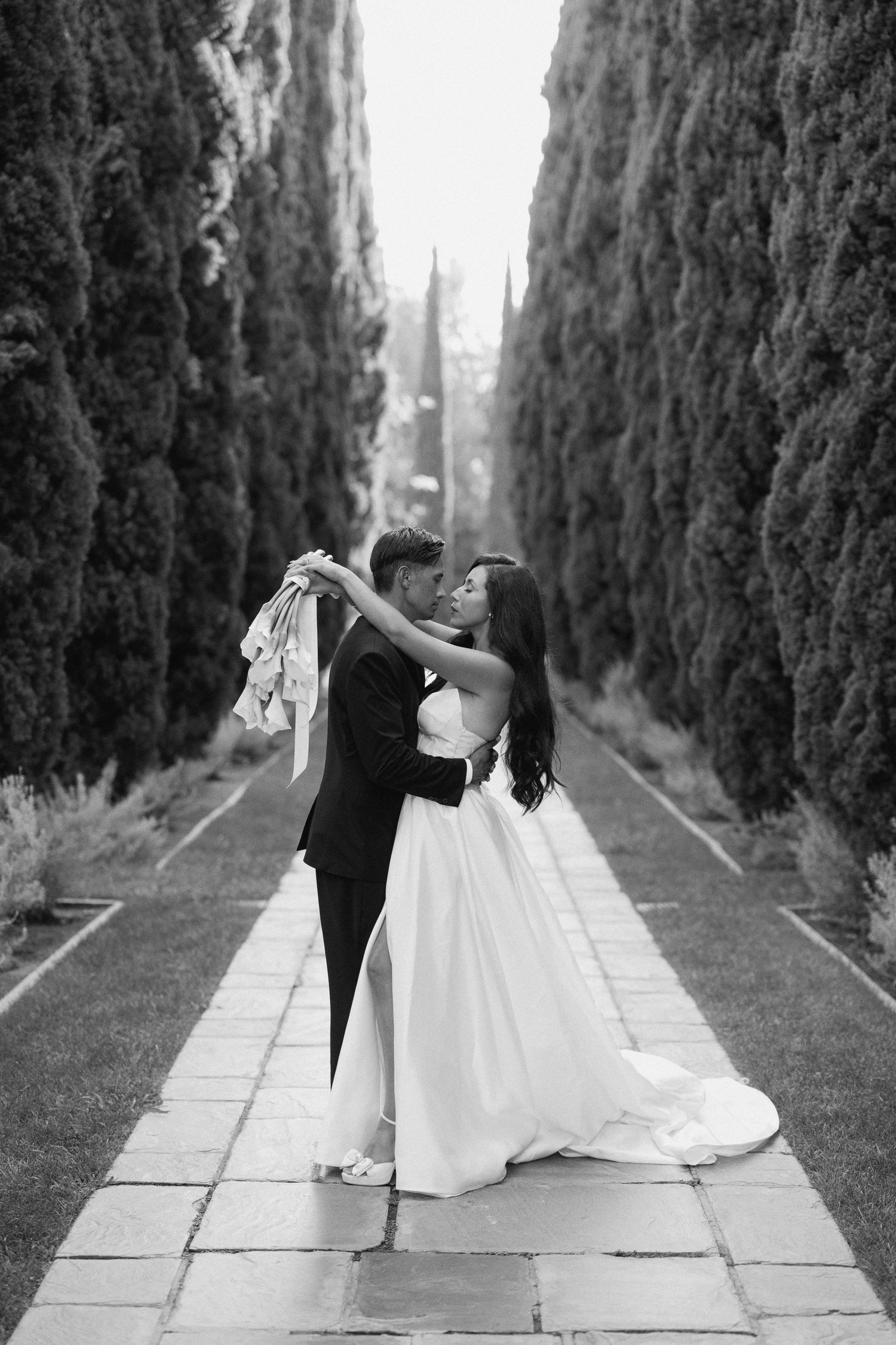 A romantic black and white photo sequence of a couple dancing in an Italian cypress-lined garden pathway.