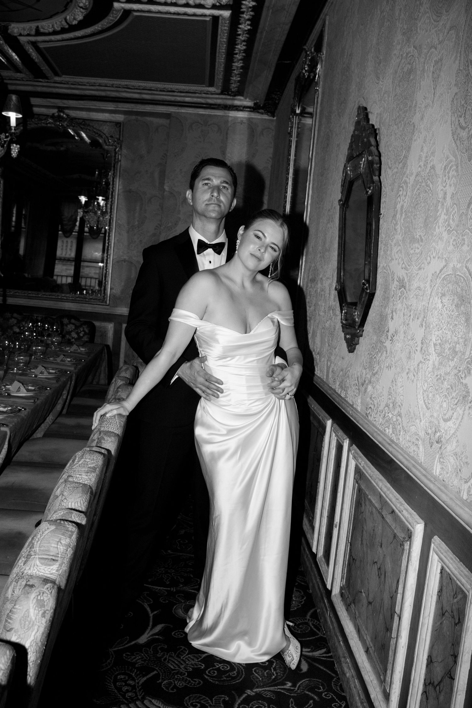 A romantic wedding couple embraces on a Parisian rooftop terrace with the iconic Eiffel Tower visible in the background.