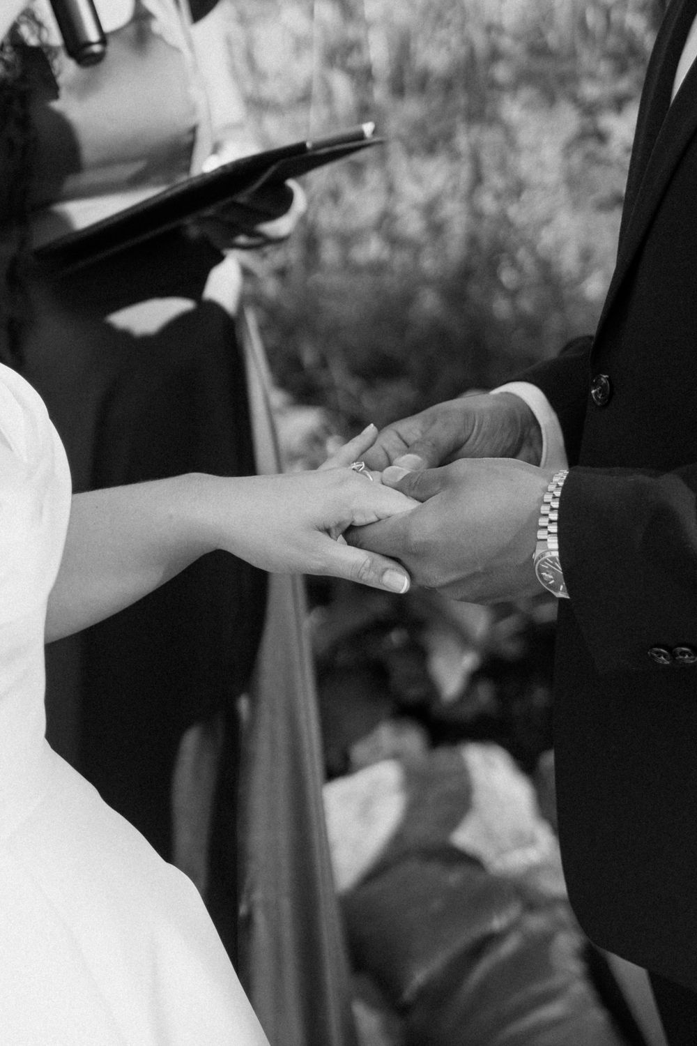 Groom places wedding ring on brides finger during outdoor ceremony in black and white.