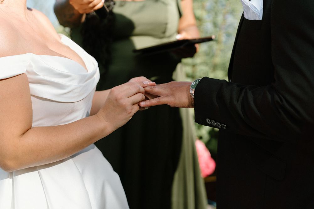 Close-up of bride and groom exchanging rings during outdoor wedding ceremony.